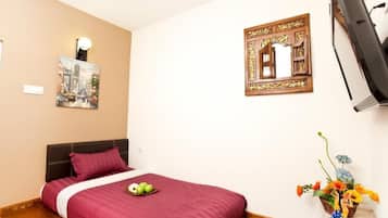 A hotel room with a bed, a wall-mounted TV, a decorative mirror, and a painting.