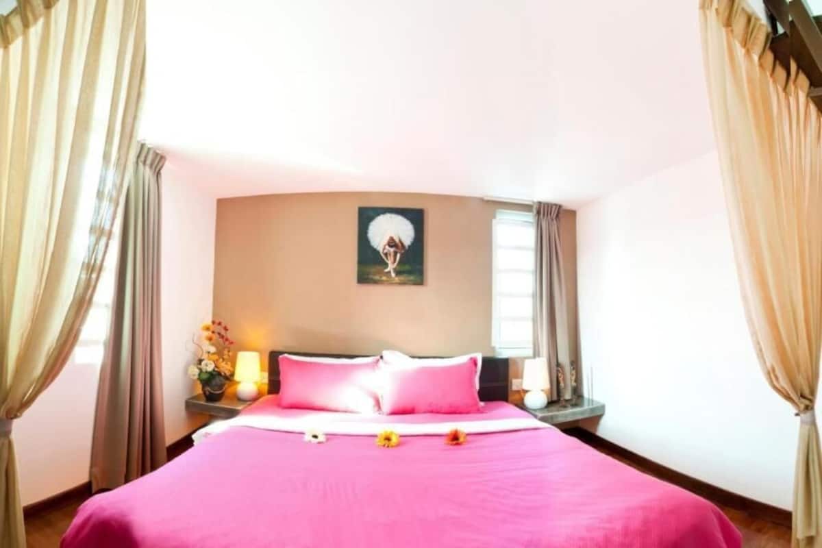 A hotel room with a large bed, a painting on the wall, and curtains on the windows.