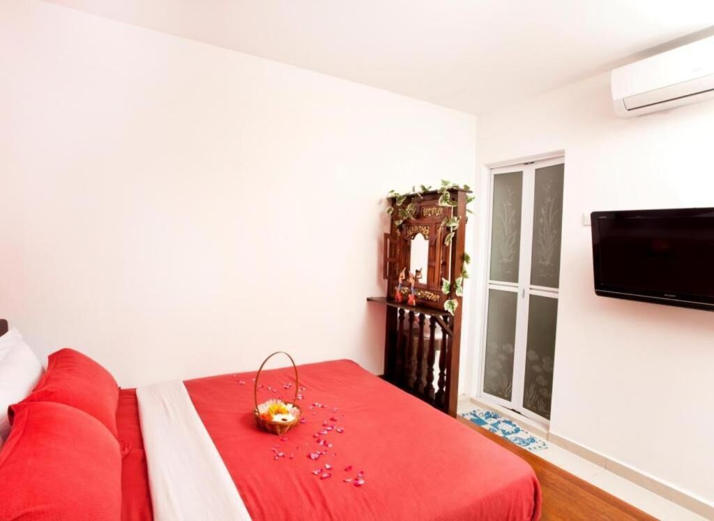 Een slaapkamer met een rode spreideken, een houten kast met planten, een televisie aan de muur en een raam met uitzicht.