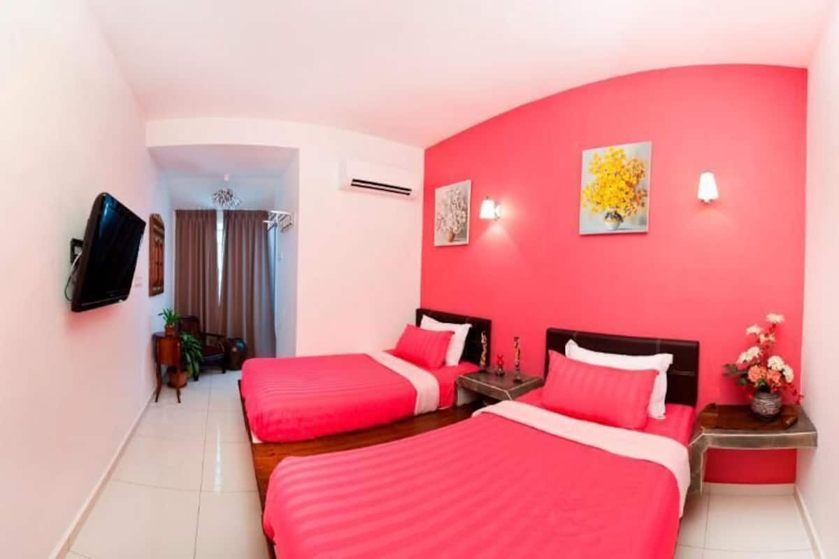 A hotel room with two beds, a TV mounted on the wall, a door with a handle, and a small table with a vase of flowers.