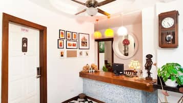 A reception area with a wooden counter, a ceiling fan, framed pictures on the wall, a clock, and a potted plant.