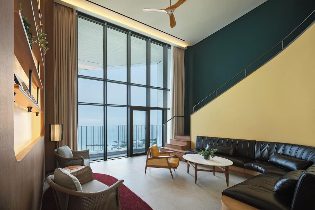 A spacious living area with a large window, a ceiling fan, and a black leather sofa.