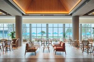 A spacious indoor area with a high ceiling, large windows, and a variety of seating arrangements including sofas and chairs.