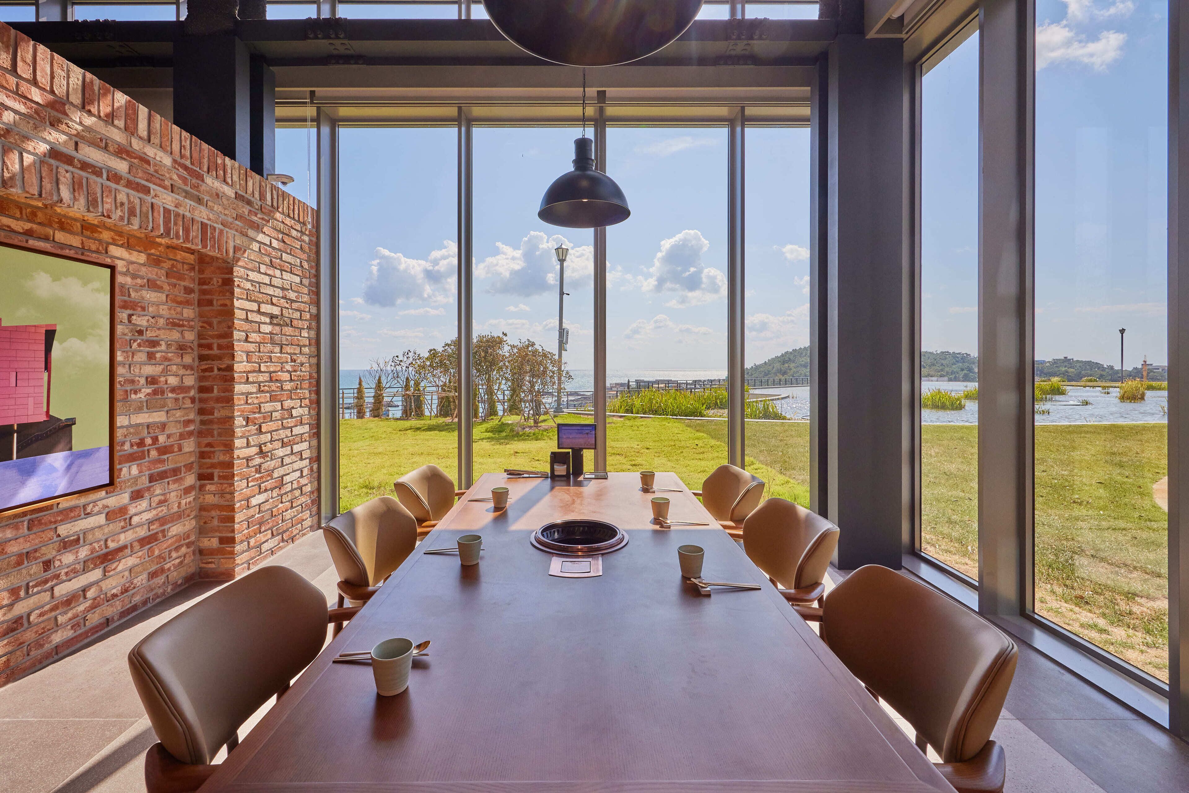 A conference room with a long table, chairs, and a large window with a view of a body of water and greenery.