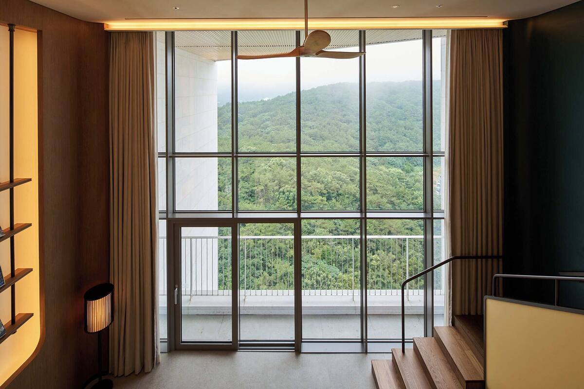 A modern hotel room with a large window offering a view of a forested mountain range.