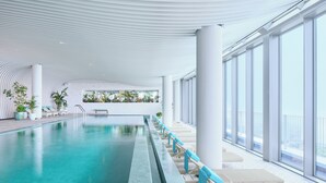 An indoor swimming pool with clear blue water, surrounded by large windows and white columns. - Ananti At Busan Village (Busan)