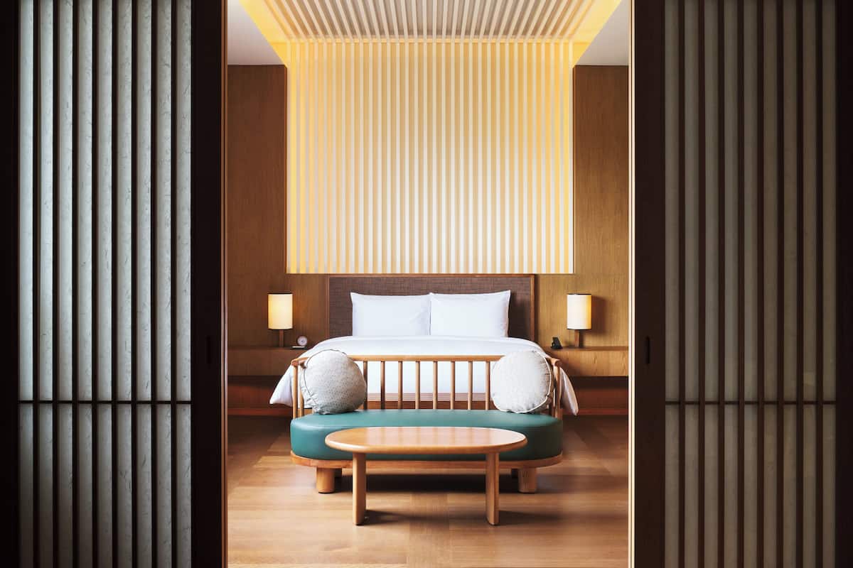 A modern hotel room with a large bed, a green sofa, and a wooden floor.