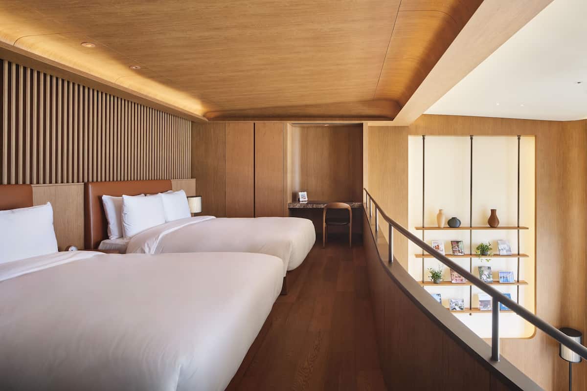 A hotel room with two beds, a desk, and a view of the city.