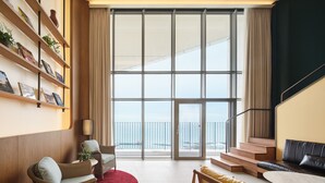 A spacious living area with a large window, a bookshelf, a red rug, and a staircase leading to an outdoor balcony. - Ananti At Busan Village (Busan)
