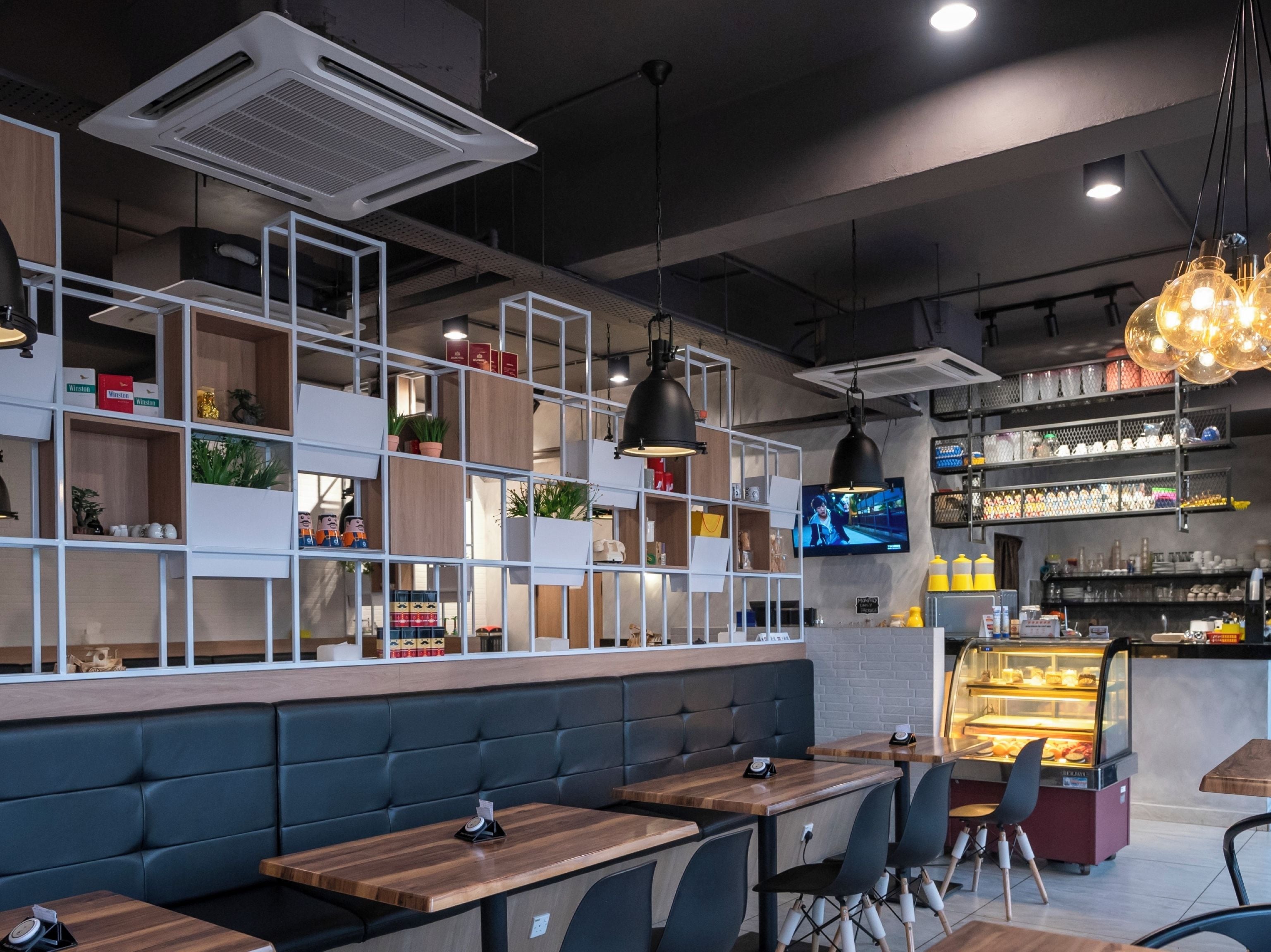 A modern cafe interior with wooden tables, black cushioned seating, and a display case with baked goods.