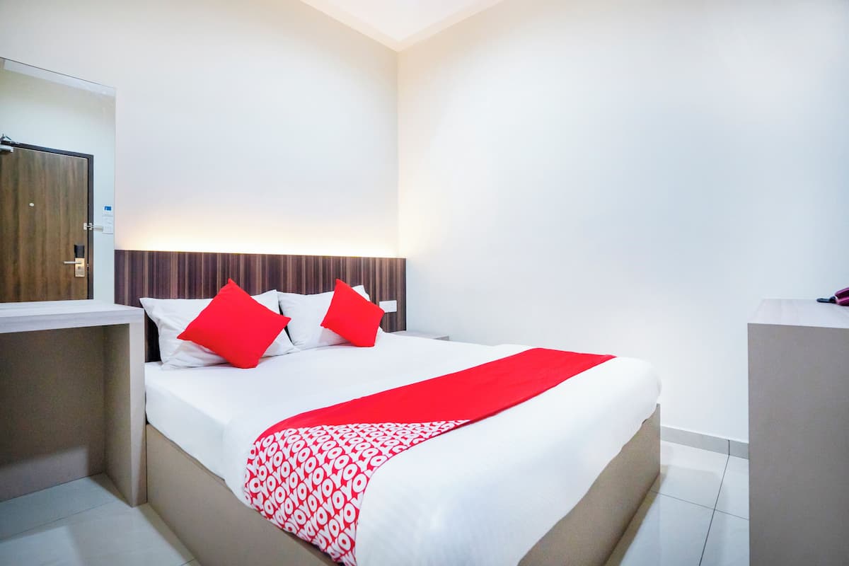 A hotel room with a bed, a bedside table, a mirror, and a wooden headboard.