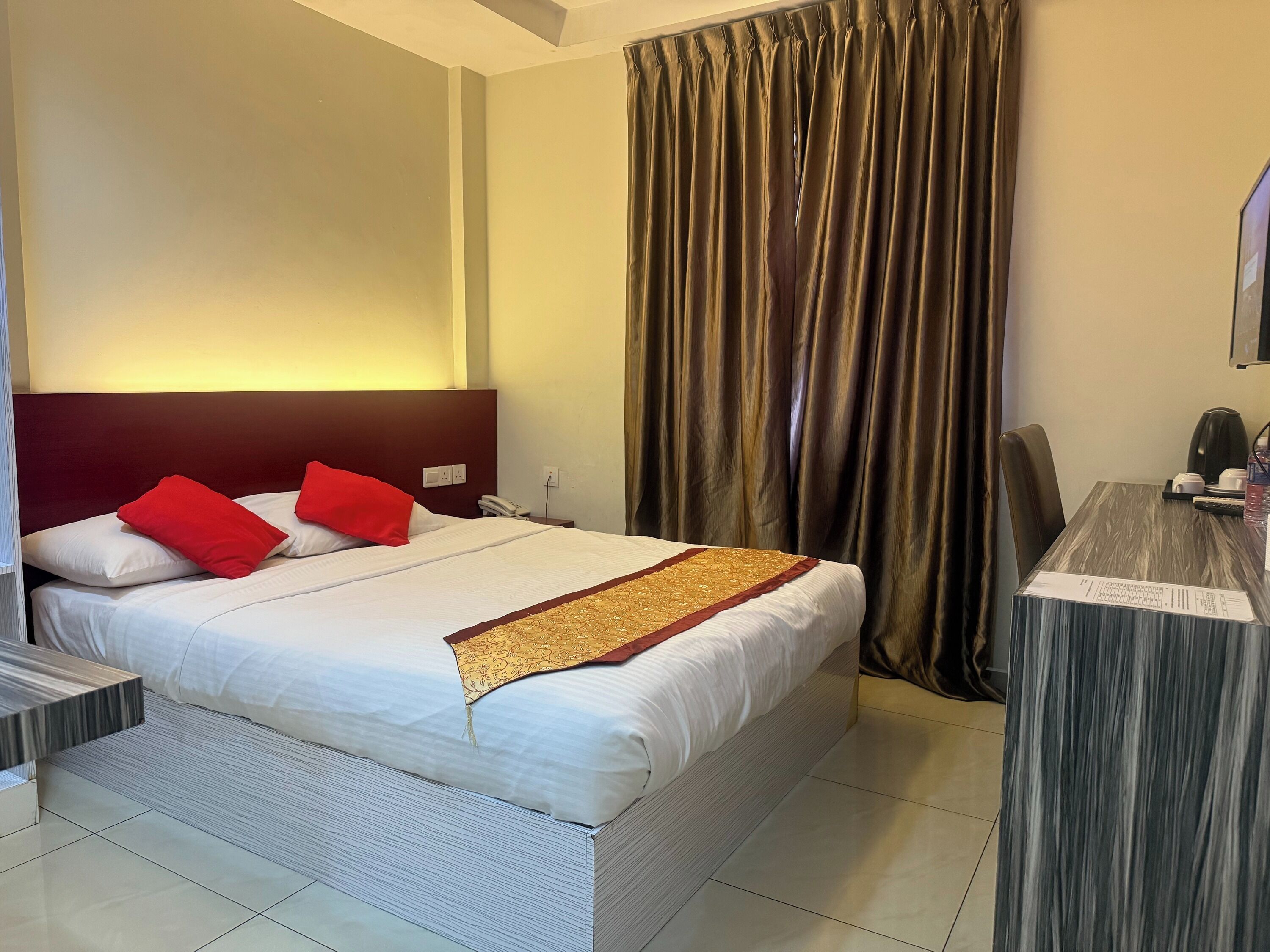 A hotel room with a bed, a desk, a chair, a telephone, and a curtain.