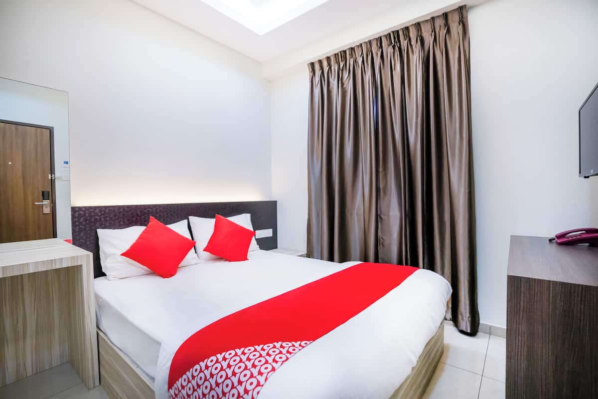 A hotel room with a bed, a desk, a television, and a window with curtains.