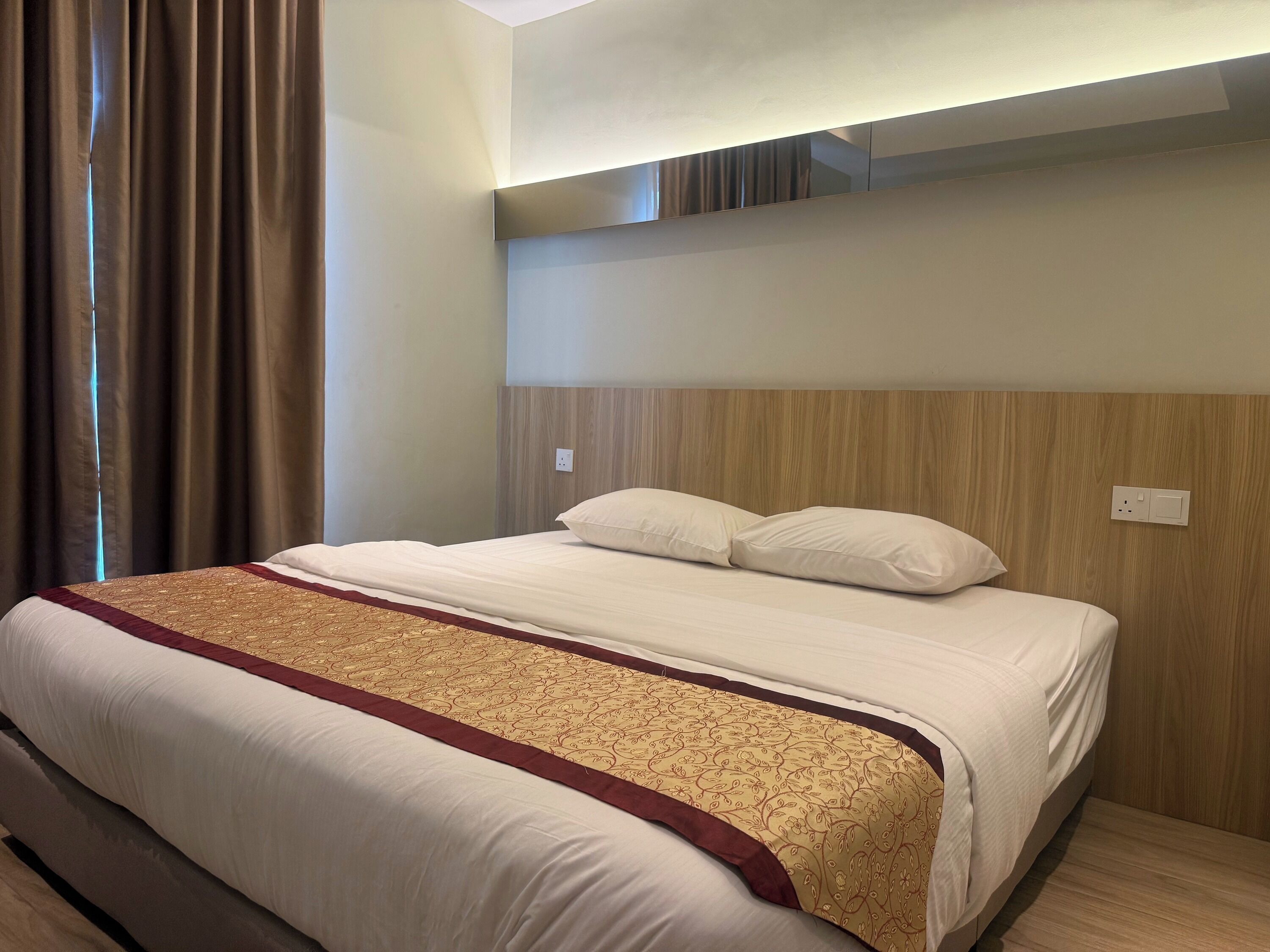 Habitación de hotel con cama, cortinas, cabecero de madera y una lámpara fijada a la pared.
