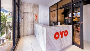 A reception desk with a marble top and a logo, a glass door leading to a seating area, and a plant visible outside. - Hope Hotel (Masai)