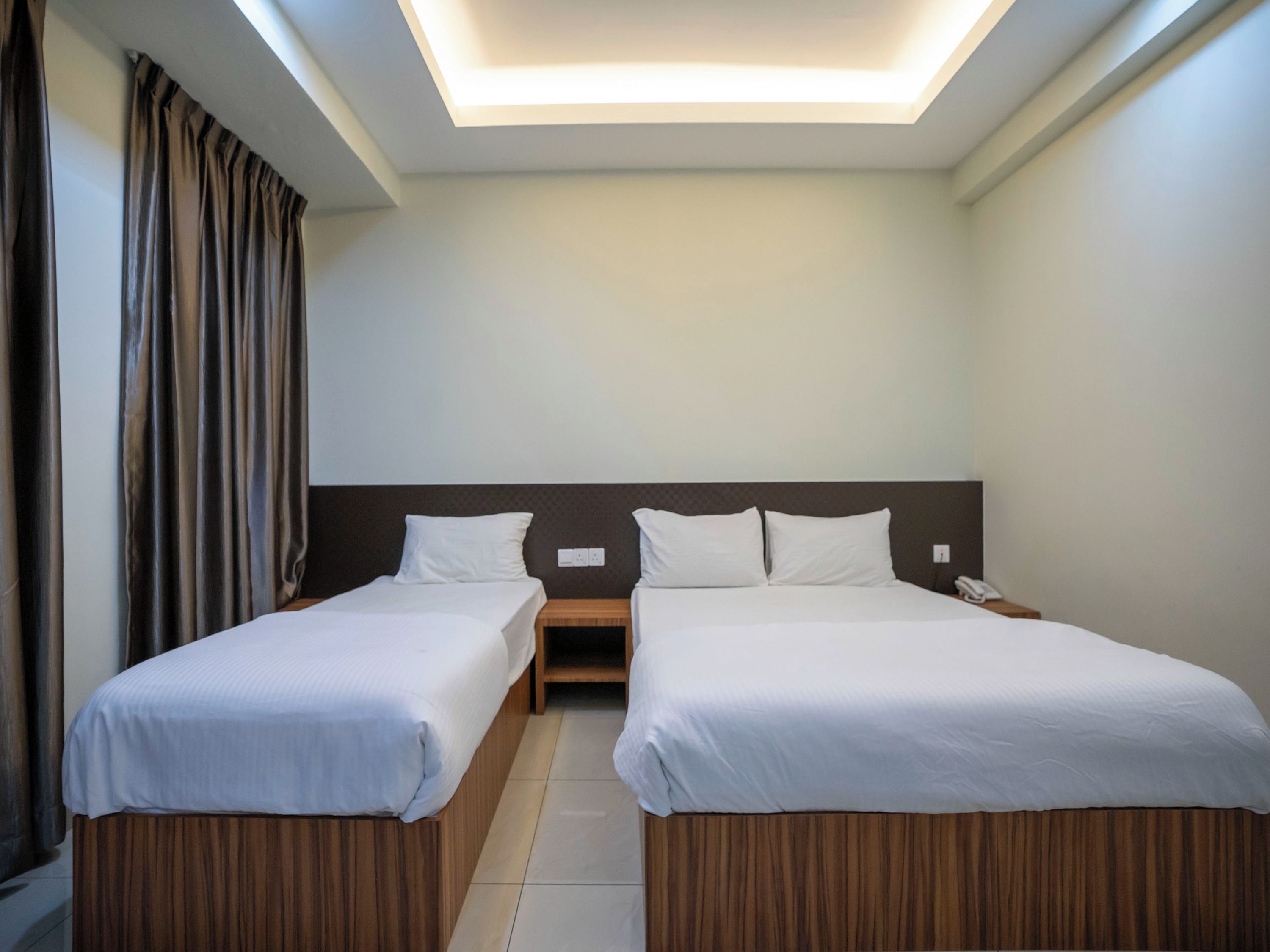 Een hotelkamer met twee bedden, een houten hoofdeinde, een nachtkastje met telefoon en een plafondlamp.