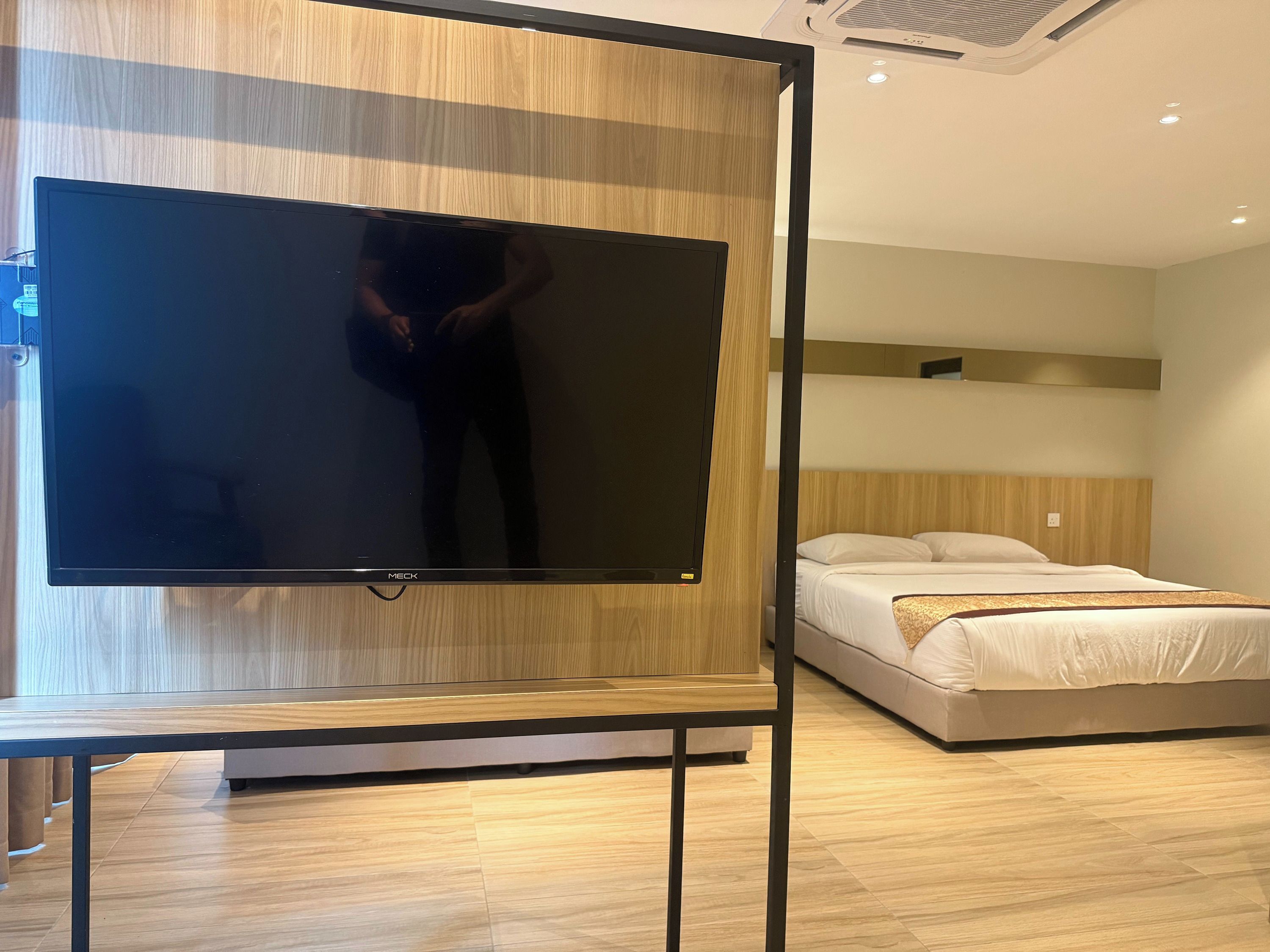 Une chambre d’hôtel dotée d’un grand téléviseur à écran plat fixé sur un panneau en bois, d’un lit avec une literie blanche et d’un plancher en bois.