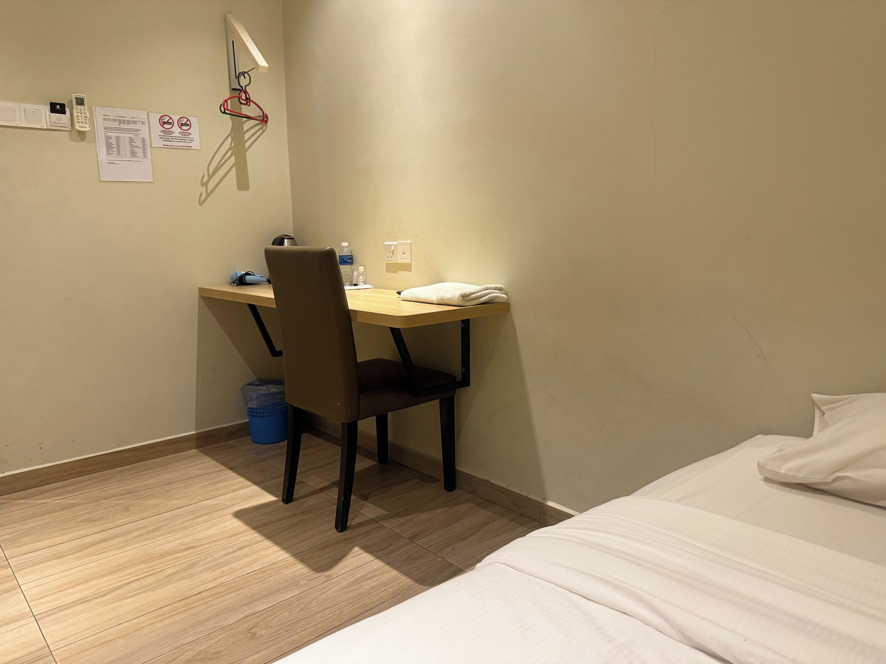 A hotel room with a wooden desk, a chair, a bed, a trash bin, and a wall-mounted telephone.