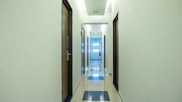 A long, narrow hallway with doors on both sides, a tiled floor with a blue and white pattern, and a ceiling with recessed lighting.