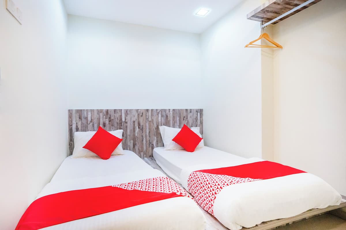 A hotel room with two beds, each with white bedding and red accents, a wooden headboard, and a wooden hanger on the wall.