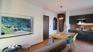 A modern kitchen with dark cabinets, a stainless steel oven, and a dining area with a wooden table and colorful chairs. - Cozy Alsace Retreat: 2BR, Sauna, Pool Access, Near Vineyards & Colmar (Rouffach)