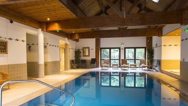 A large indoor swimming pool with clear water, wooden beams on the ceiling, and several lounge chairs around the pool area. - Cozy Alsace Retreat: 2BR, Sauna, Pool Access, Near Vineyards & Colmar (Rouffach)