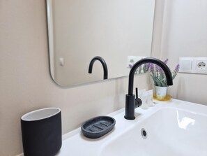 Un lavabo de salle de bain avec un robinet noir, un porte-savon noir et une tasse noire.