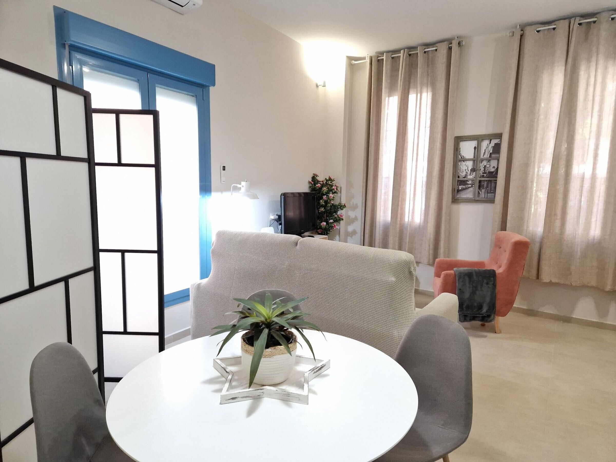 Una sala de estar con un sofá, una mesa de comedor con sillas, una planta en maceta y un televisor.