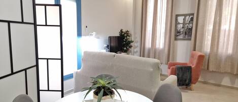 A living room with a sofa, a dining table with chairs, a potted plant, and a television.