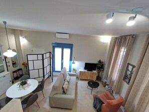 Una sala de estar moderna con un sofá, una mesa de comedor con sillas, un mueble para la televisión y una mesita con un control remoto.