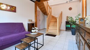 A living room with a purple sofa, a wooden coffee table, a staircase, and a kitchen area with a bar sign. - Beautiful Country Home with Terrace, Close to Amenities & Highways, Sleeps 5 + Baby (Baldersheim)
