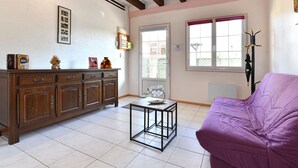 A room with a wooden cabinet, a purple sofa, a small table, and a window with a view of buildings. - Beautiful Country Home with Terrace, Close to Amenities & Highways, Sleeps 5 + Baby (Baldersheim)