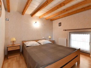 Un dormitorio con cama de madera, dos mesitas de noche, una lámpara de pared, un radiador y una ventana con vistas.