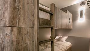 Una cama litera con estructuras de madera y ropa de cama blanca, una lámpara fijada a la pared y suelo de madera.