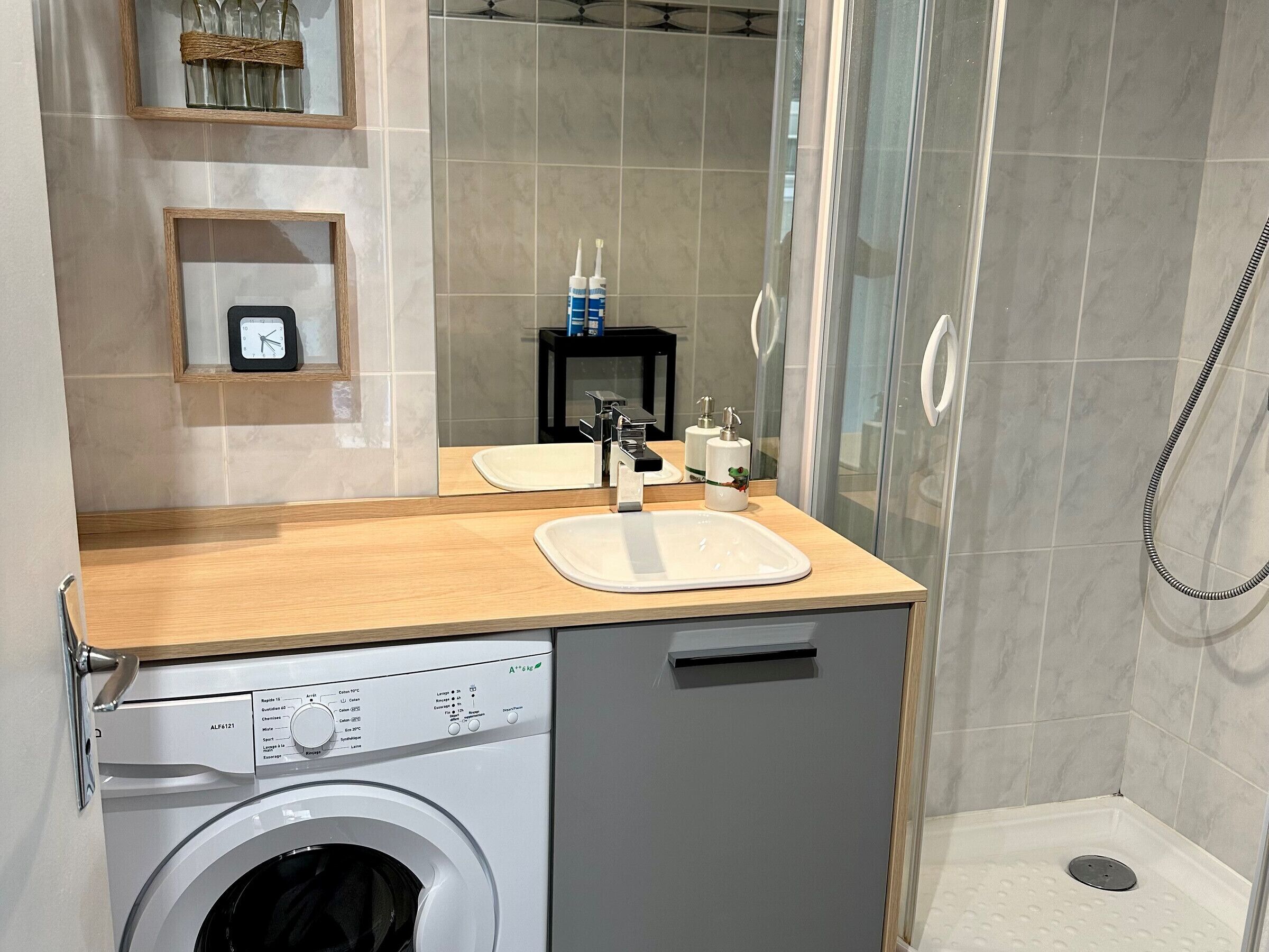 A compact bathroom with a washing machine, two sinks, a mirror, and a shower area.
