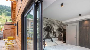 A modern bedroom with a large bed, a glass door leading to a balcony, and a mountain view. - Luxurious Apartment with WiFi & Garage - Ski-In/Ski-Out, New Residence (Val-d'Isère)