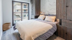A modern bedroom with a large bed, wooden wardrobe, and a view of a building through a glass door. - Luxurious Apartment with WiFi & Garage - Ski-In/Ski-Out, New Residence (Val-d'Isère)