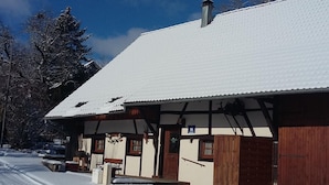 A snow-covered building with a traditional design, featuring a wooden facade and a sloped roof. - Charming Alsatian Farmhouse: 2 Terraces, BBQ, Accessible, Near Vosges – Sleeps 6 (Bretten)