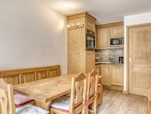 A wooden dining table with chairs, a kitchen with wooden cabinets, and a microwave.