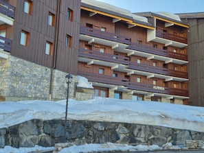 Un hôtel à plusieurs étages doté de balcons, de murs en pierre et surplombant un paysage enneigé.