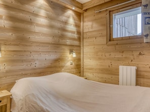 A wooden cabin room with a bed, a window, and a radiator.