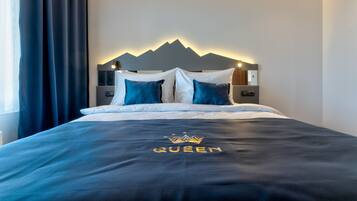 Un letto rifatto con una coperta e dei cuscini blu scuro, un poggiatesta fissato al muro con la silhouette di una montagna e un comodino con una lampada.