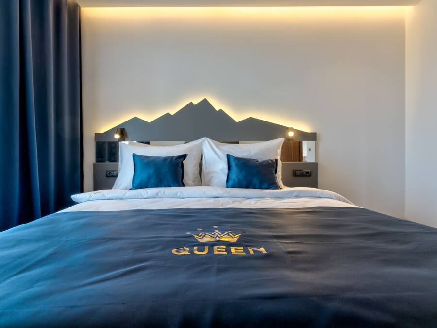 Un letto rifatto con una coperta e dei cuscini blu scuro, un poggiatesta fissato al muro con la silhouette di una montagna e un comodino con una lampada.