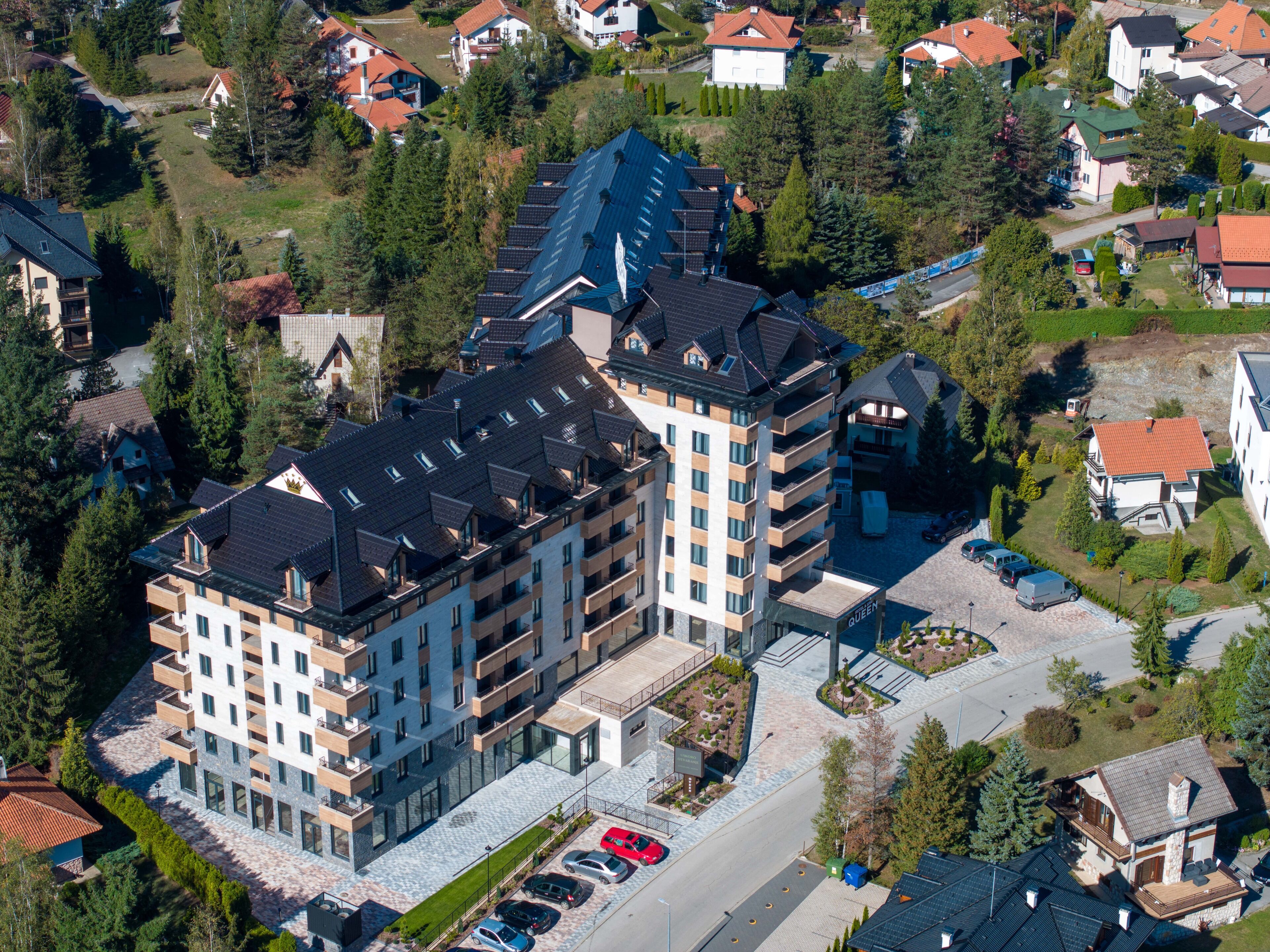 Un hôtel à plusieurs étages, doté d’un design moderne, comprenant une cour intérieure et un parking pouvant accueillir plusieurs voitures.