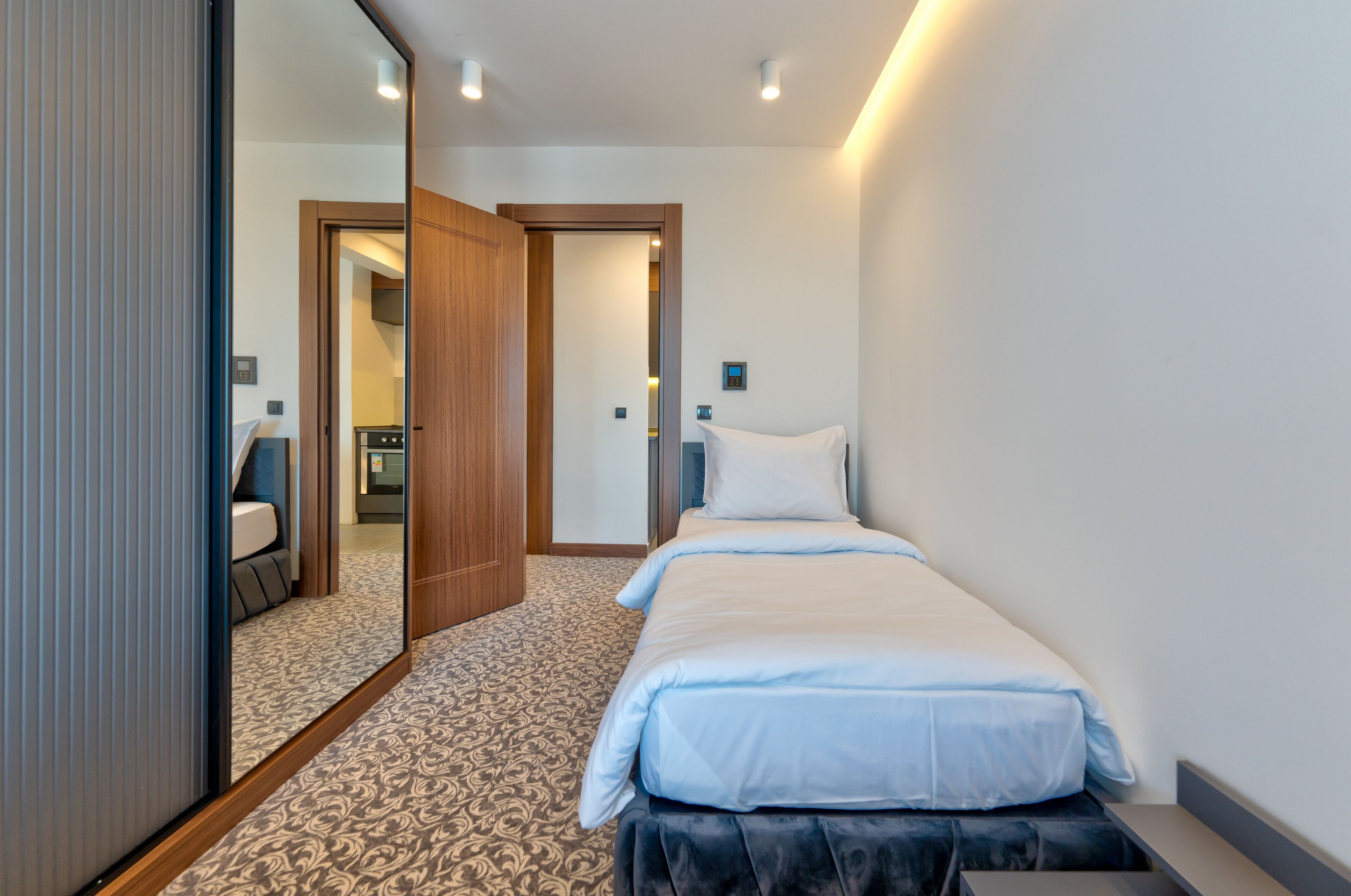 A hotel room with a bed, a mirror, a wardrobe, and a carpeted floor.