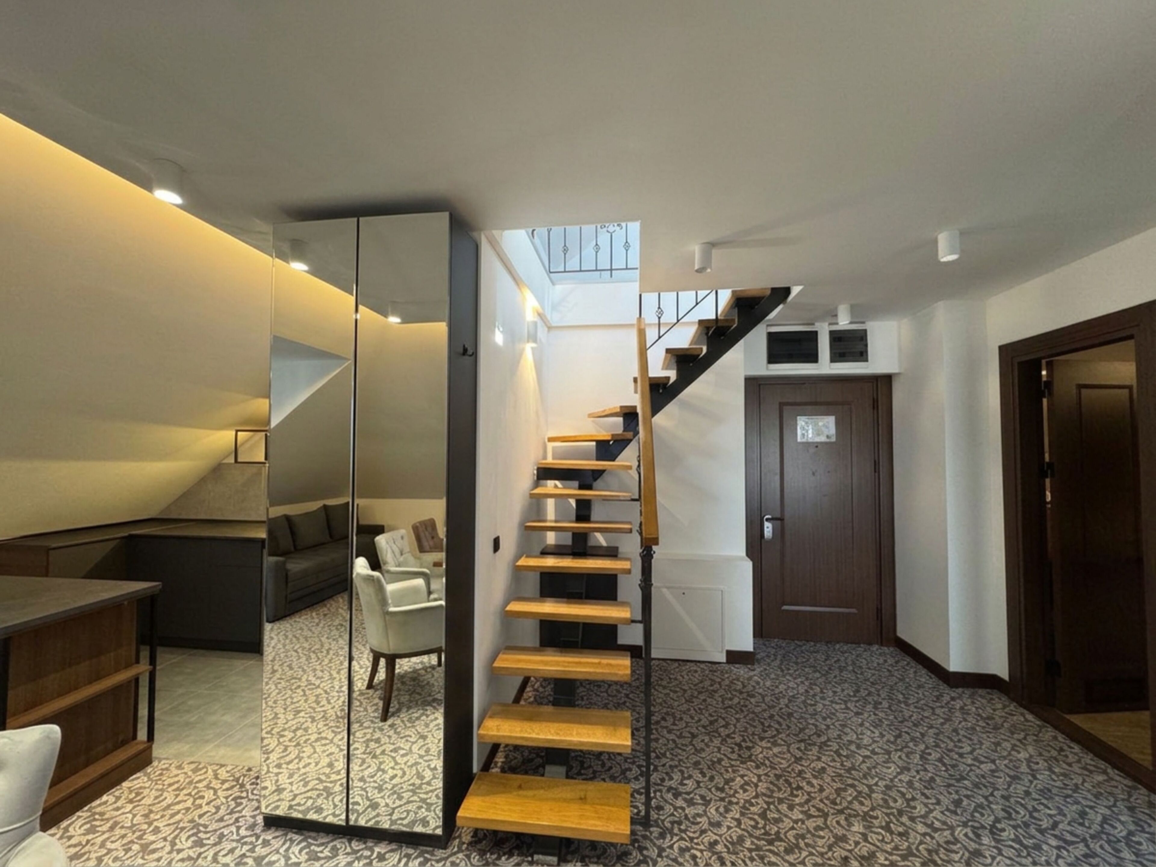 Un intérieur moderne avec un escalier, un canapé et un miroir qui reflète l’espace.