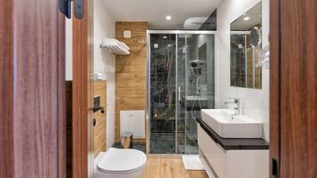 Un baño moderno con cabina de ducha de vidrio, inodoro blanco y tocador con lavamanos.
