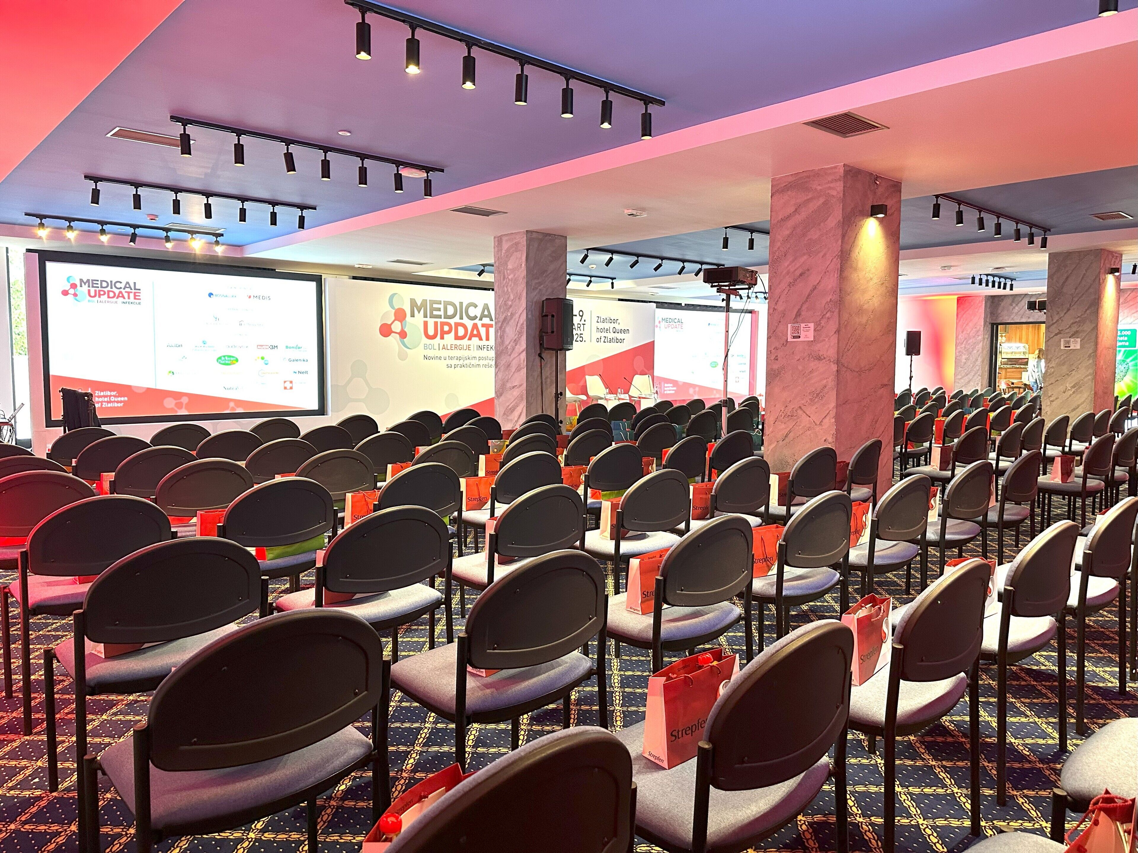 A conference room with rows of chairs and a presentation screen displaying 'MEDICA UPDATE'.