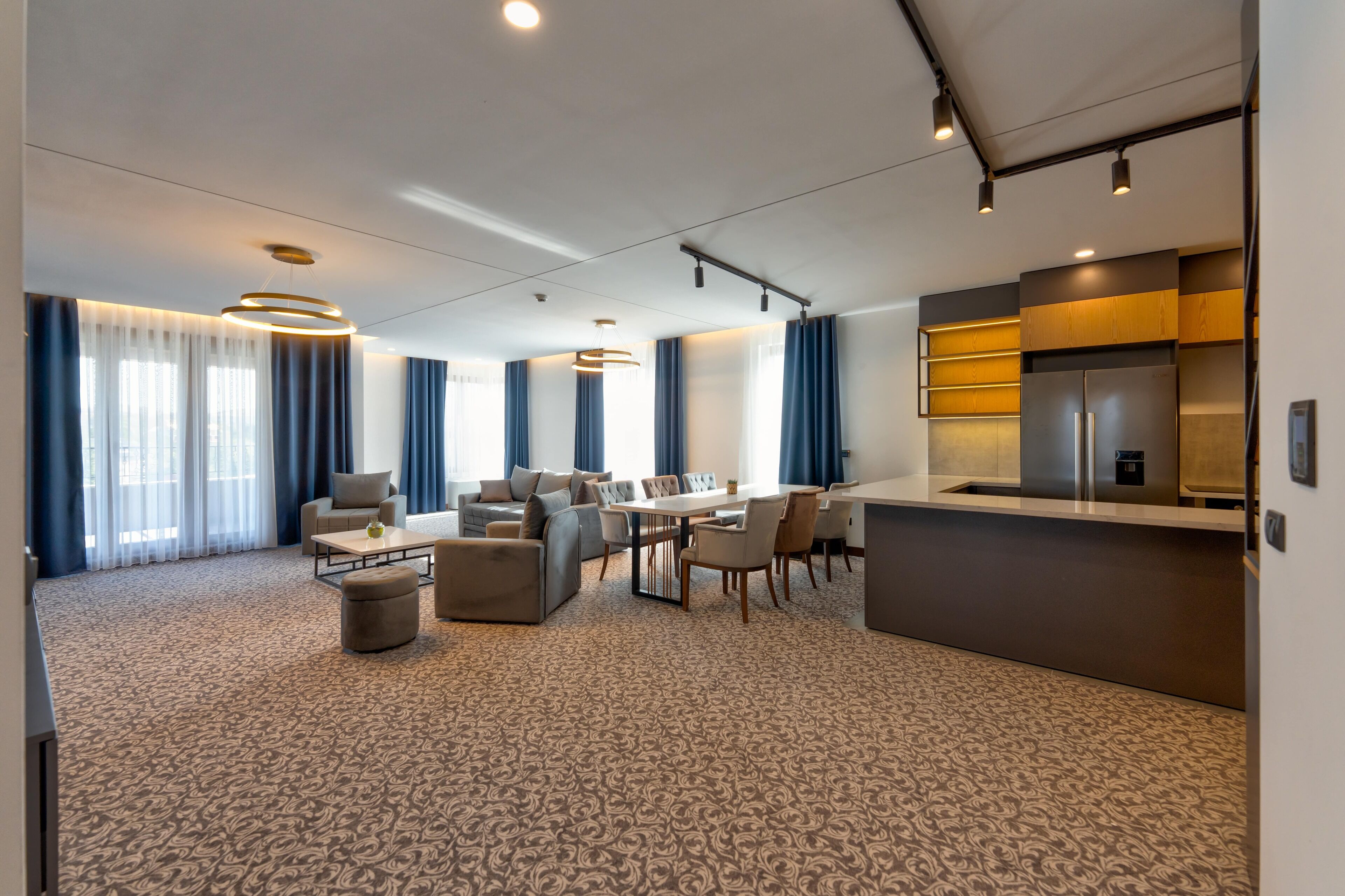 A modern hotel room with a dining area, a sofa, a coffee table, and a kitchen counter.
