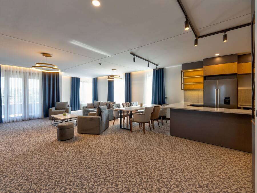 A modern hotel room with a dining area, a sofa, a coffee table, and a kitchen counter.
